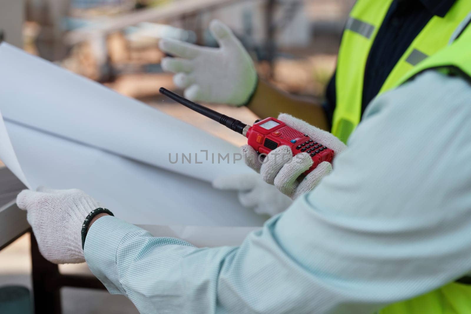 A construction worker wearing gloves and high-visibility gear studies blueprints while preparing to communicate about sustainable building practices, embodying commitment to eco-friendly initiatives.
