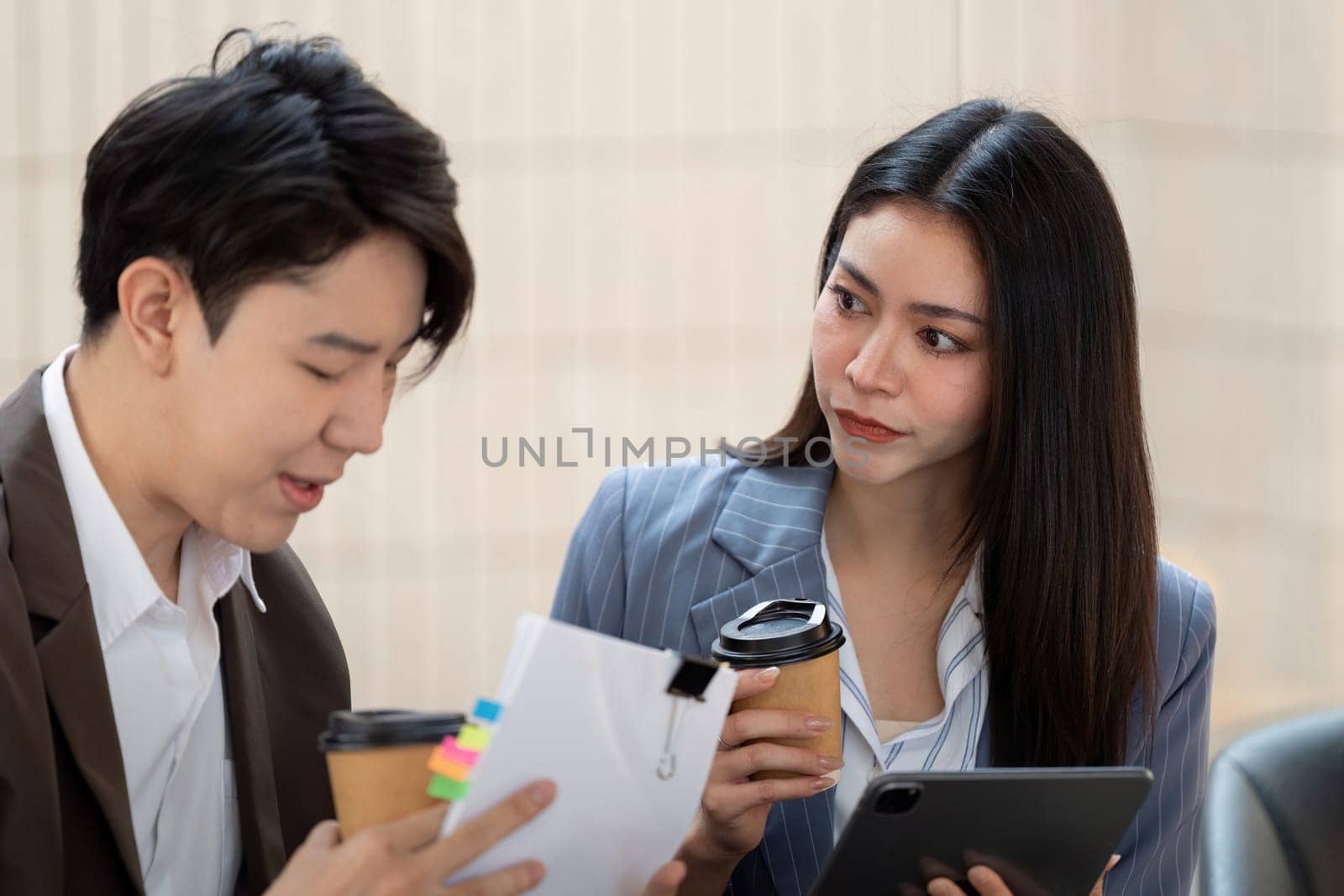 A male and female colleague engage in a thoughtful conversation, reviewing notes and planning strategies with coffee cups nearby, emphasizing teamwork and collaboration.