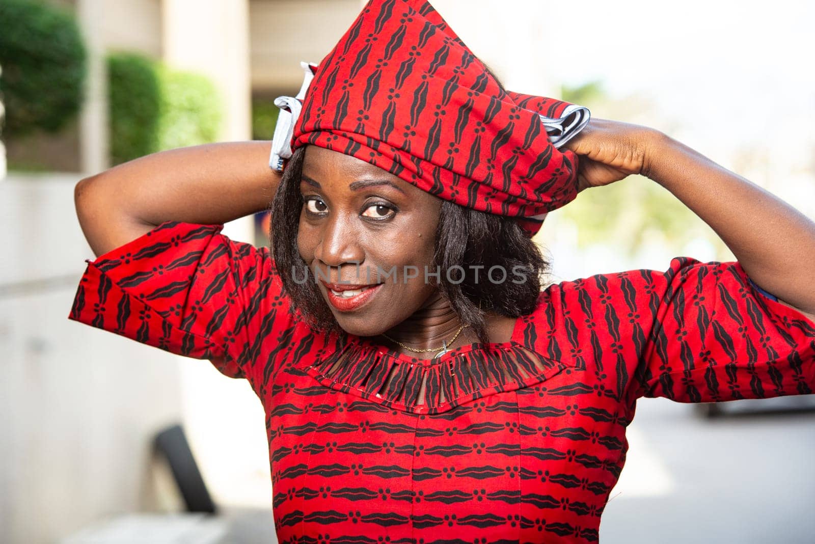 fashionable stylish african woman wearing a red loincloth straps a scarf on her head while smiling in the street in daylight