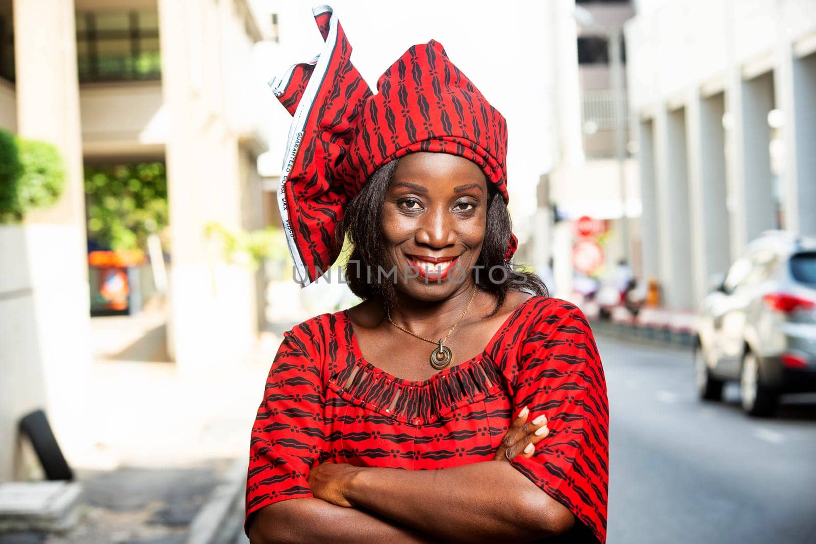 mature african woman standing outdoors head tied with a piece of loincloth watching the camera smiling.