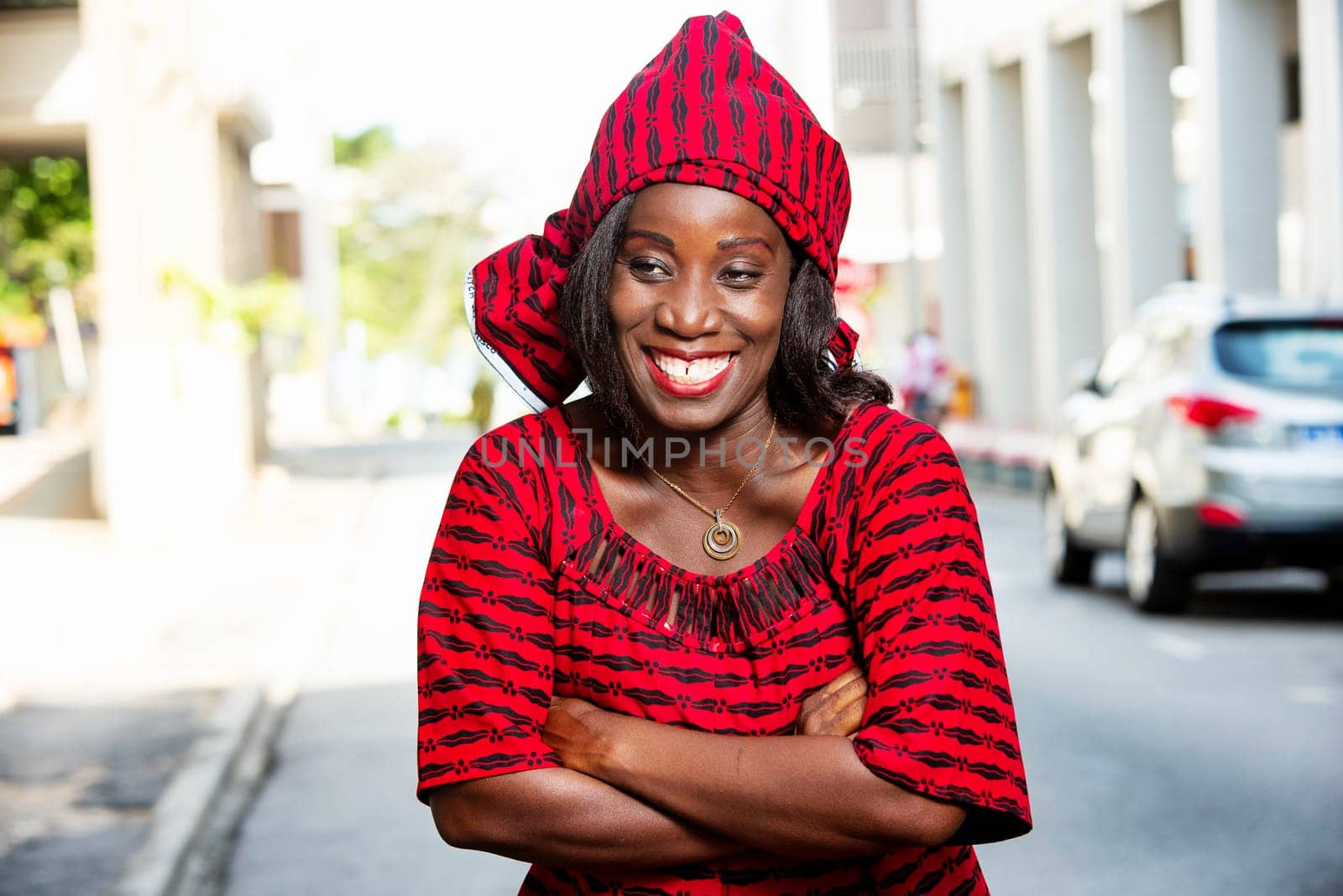 mature african woman standing outdoors head tied with a piece of loincloth watching the camera smiling.