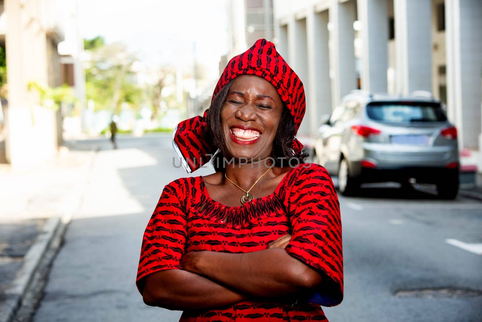 mature african woman standing outdoors head tied with a piece of loincloth watching the camera laughing.