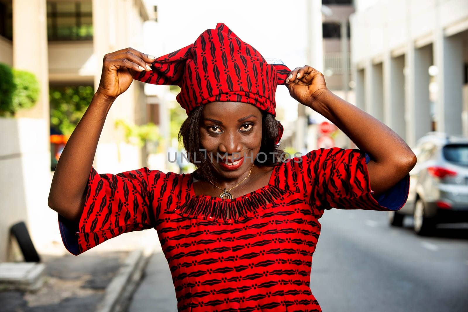 mature african woman standing outdoors adjusting her scarf and looking at camera smiling.