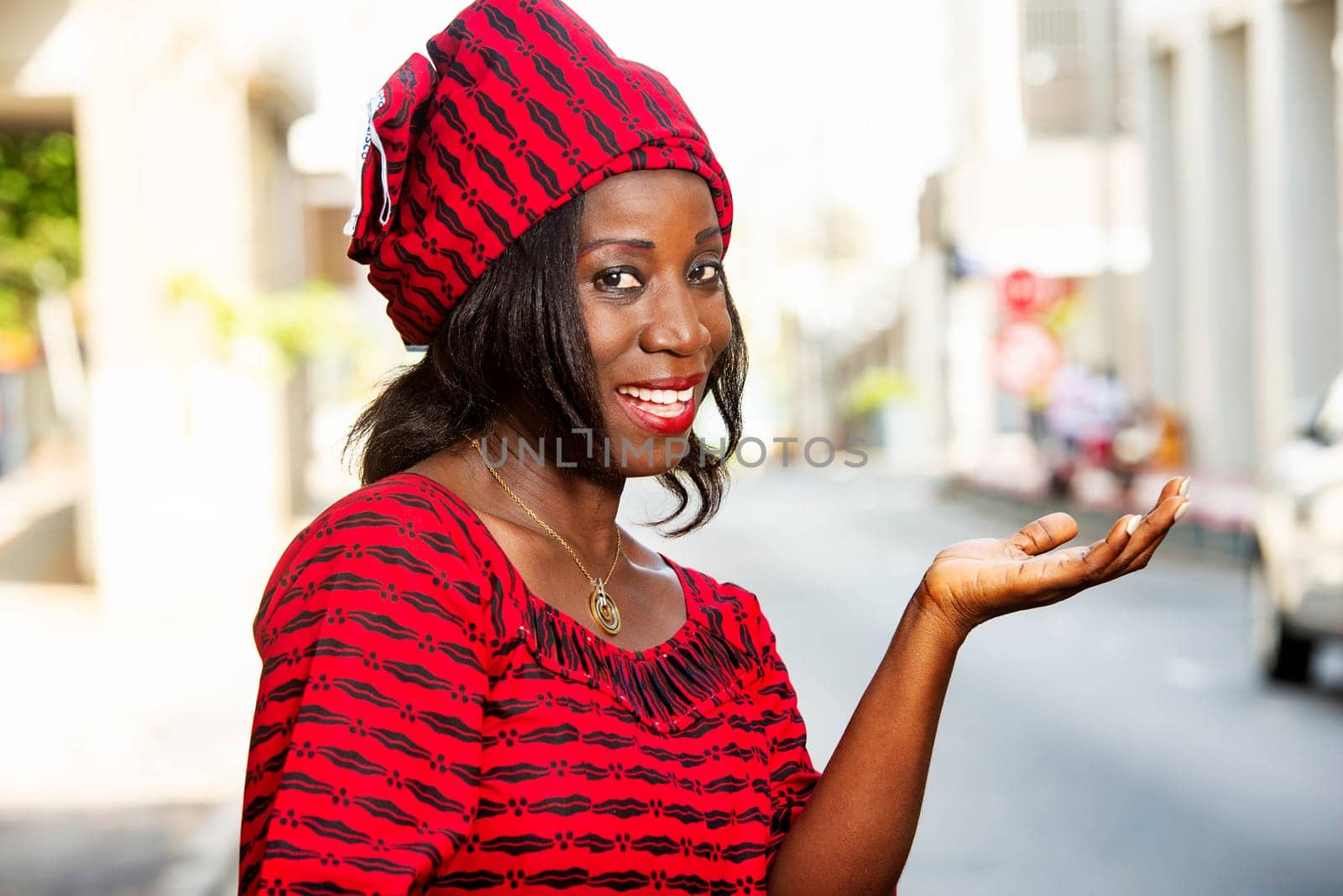 mature african woman standing outdoors looking at the profile camera smiling with outstretched hand.