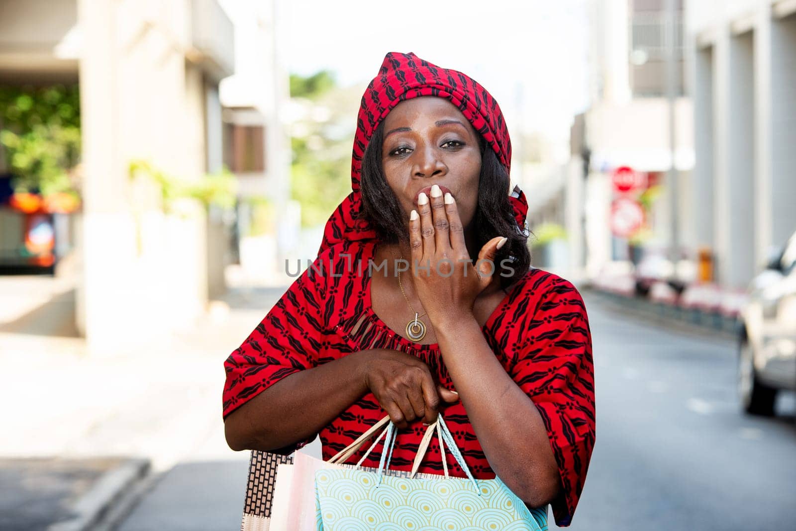 happy woman shopping in town, holding bags and making signs with her hand over her mouth while looking at the camera. Sales, consumption and people concept.