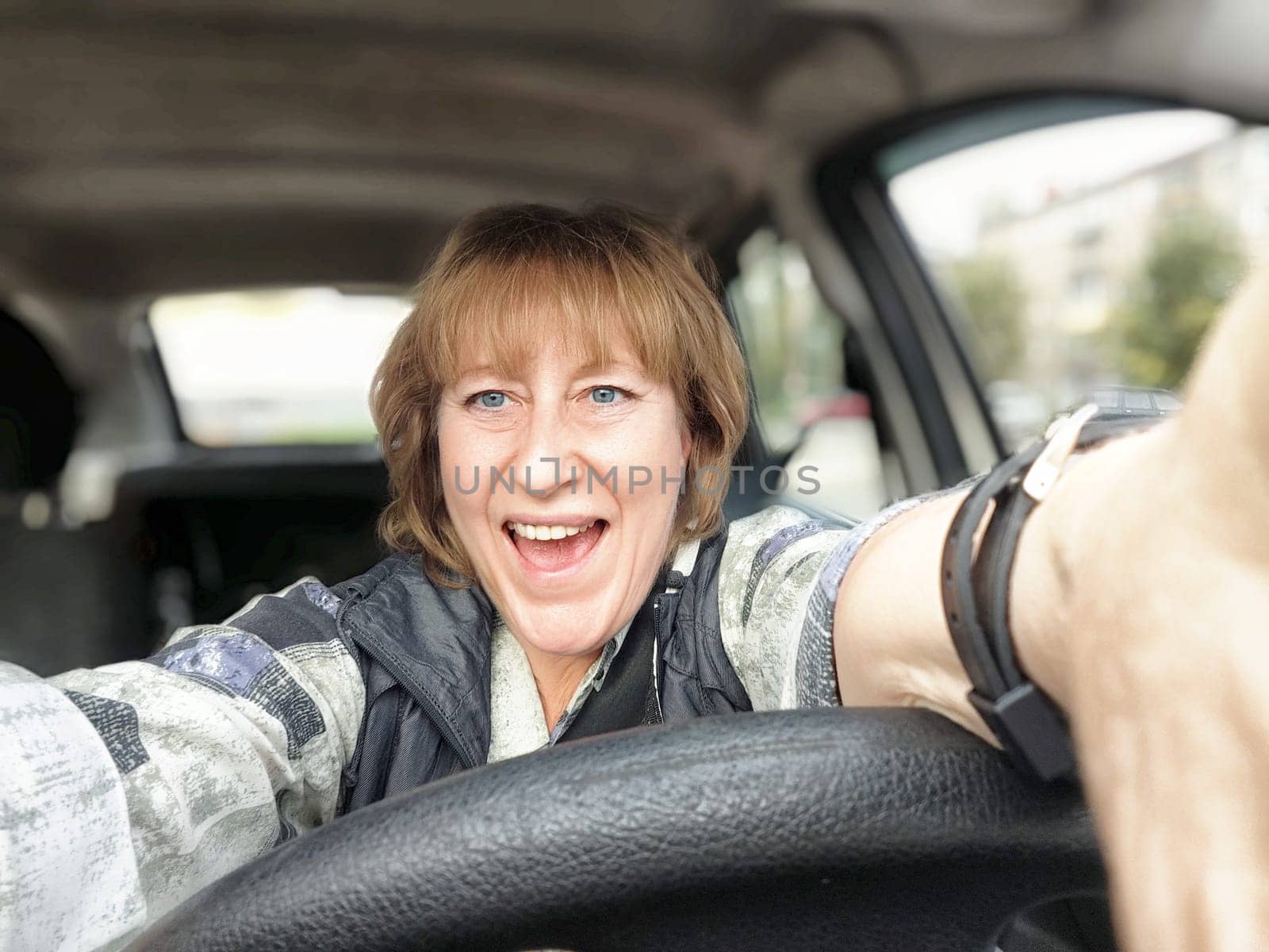 Mature woman enthusiastically drives her car while enjoying her travel excursion and capturing a selfie.