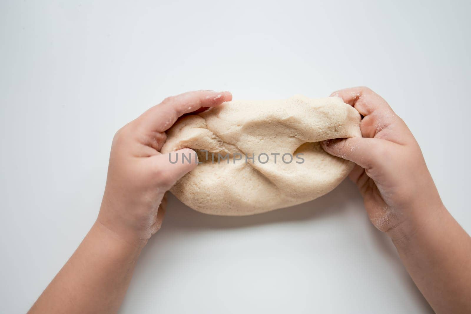 Child hands kneading dough on white surface.