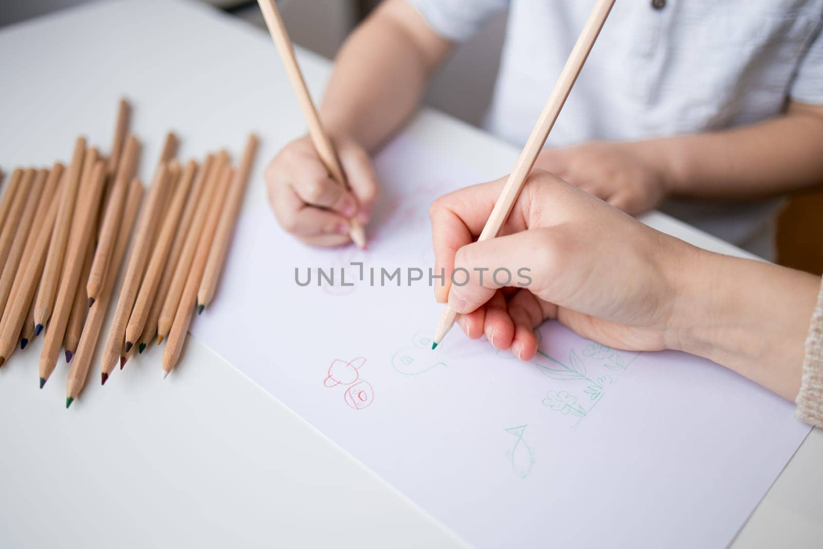 Young child and adult drawing with colored pencils on paper.