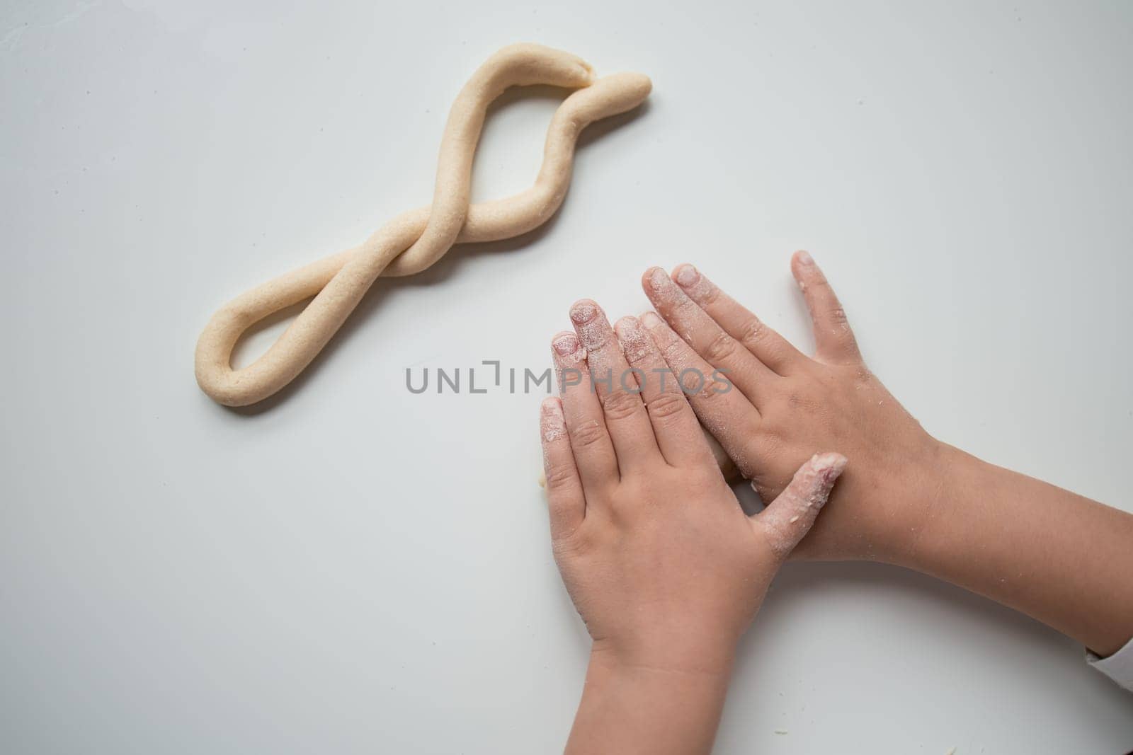 Child forming dough twist with hands in baking activity.