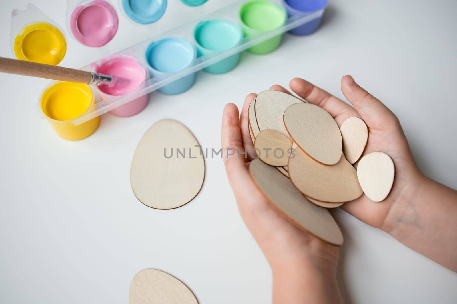 Child holding wooden Easter eggs with colorful paint set for creative crafting.