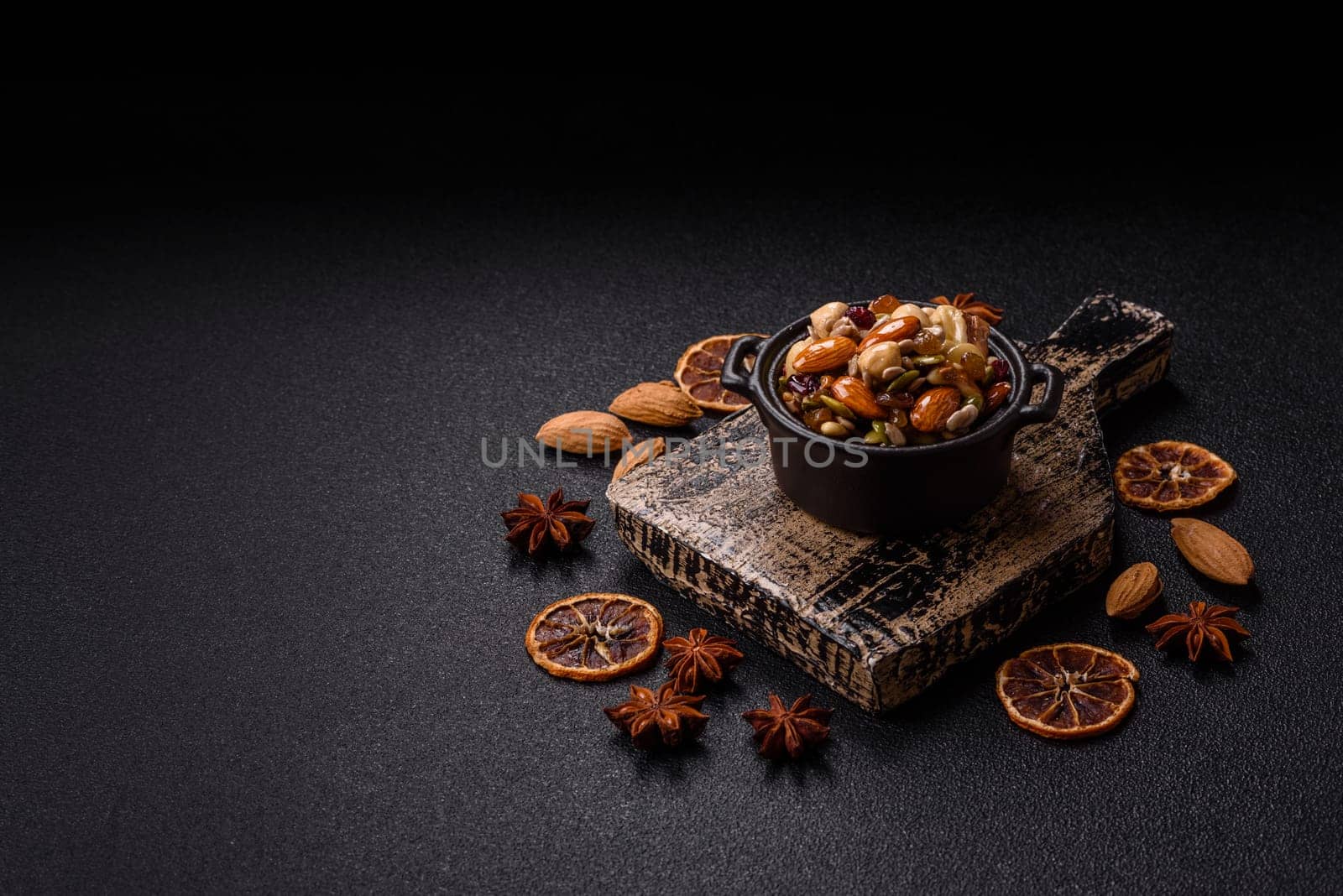 Honeyed cashew nuts, walnuts, hazelnuts, pine nuts and dried fruits in ceramic bowl on dark concrete background