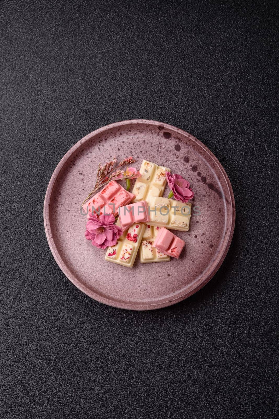 Multicolored handmade chocolate bars pink, white, brown on dark concrete background