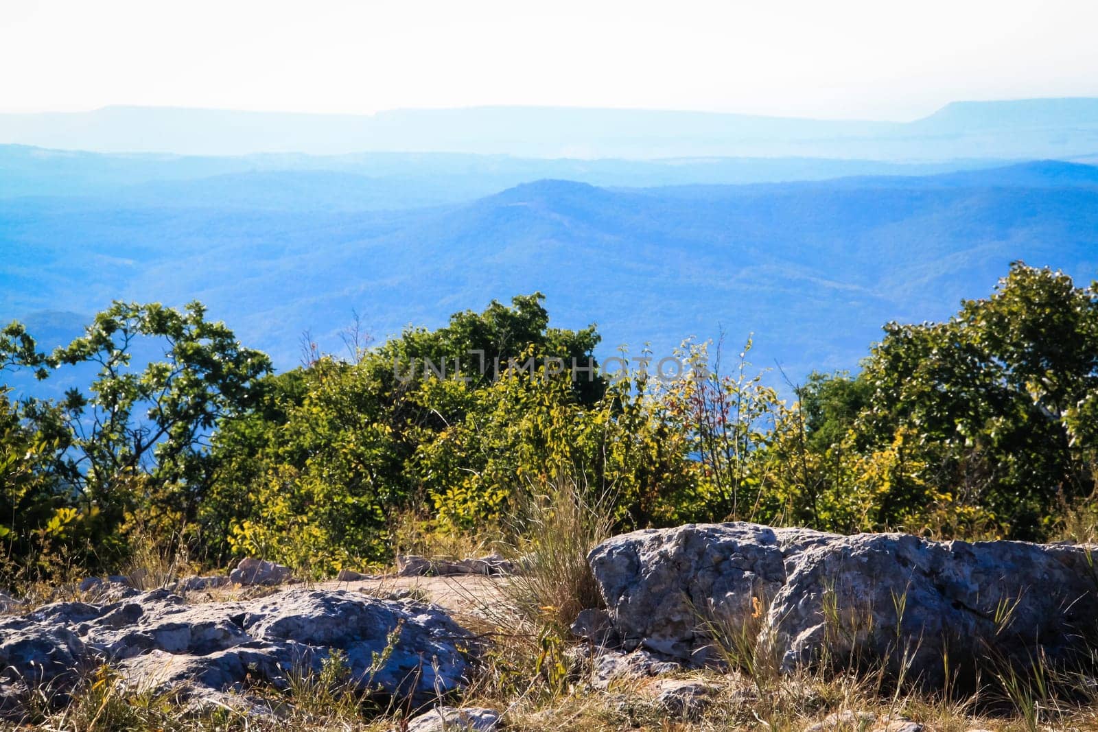 Vermont green mountain landscape views. A mountain range with a blue sky in the background. The trees are green and the rocks are grey