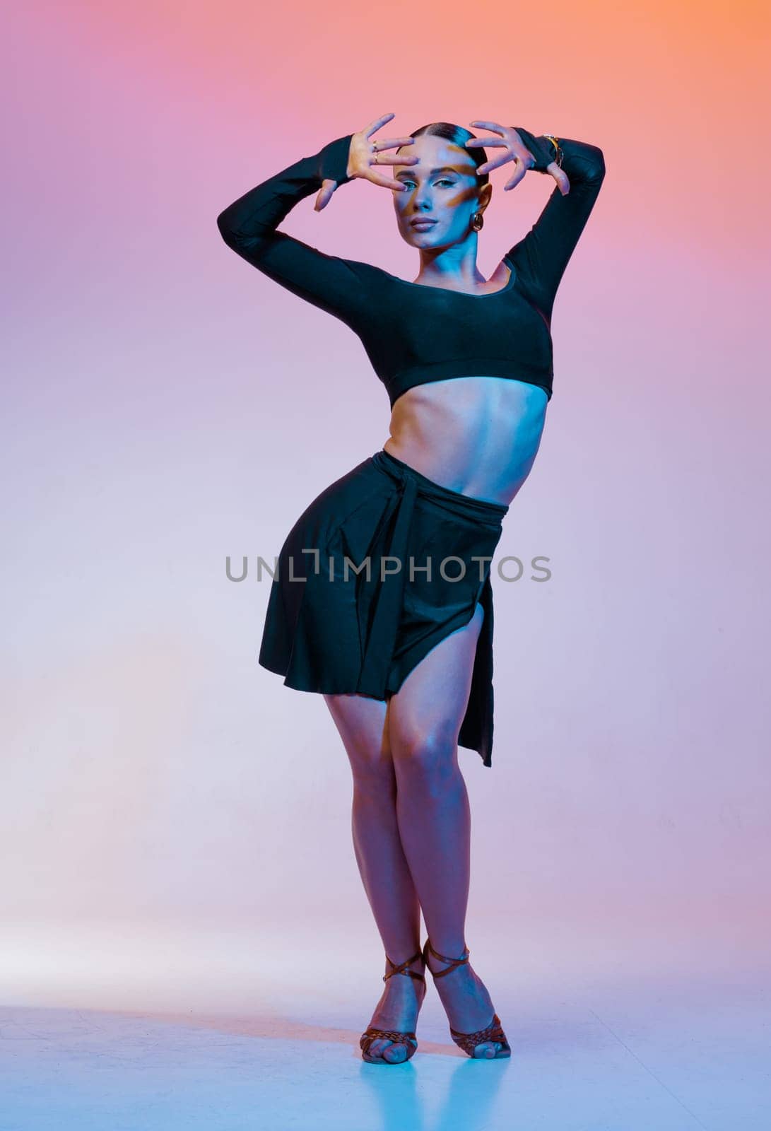 Stylish female dancer in black outfit posing in Latin dance move on vibrant gradient studio background.