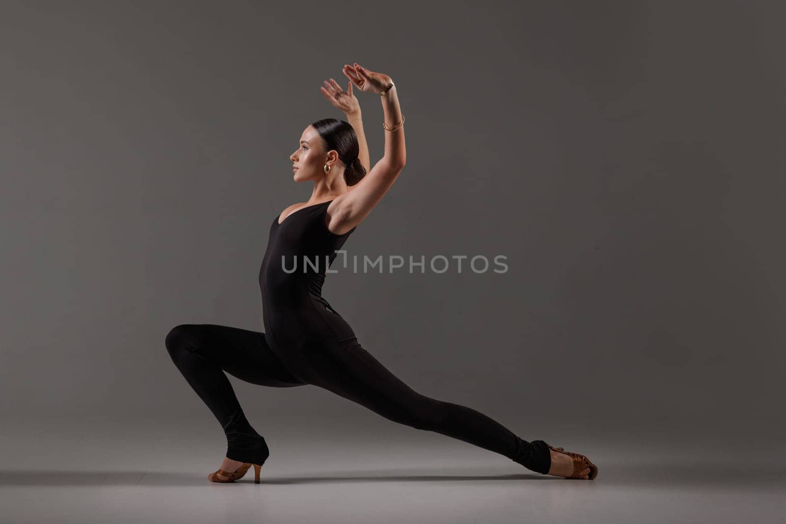 Female dancer in black bodysuit performing contemporary Latin dance pose on gray studio,