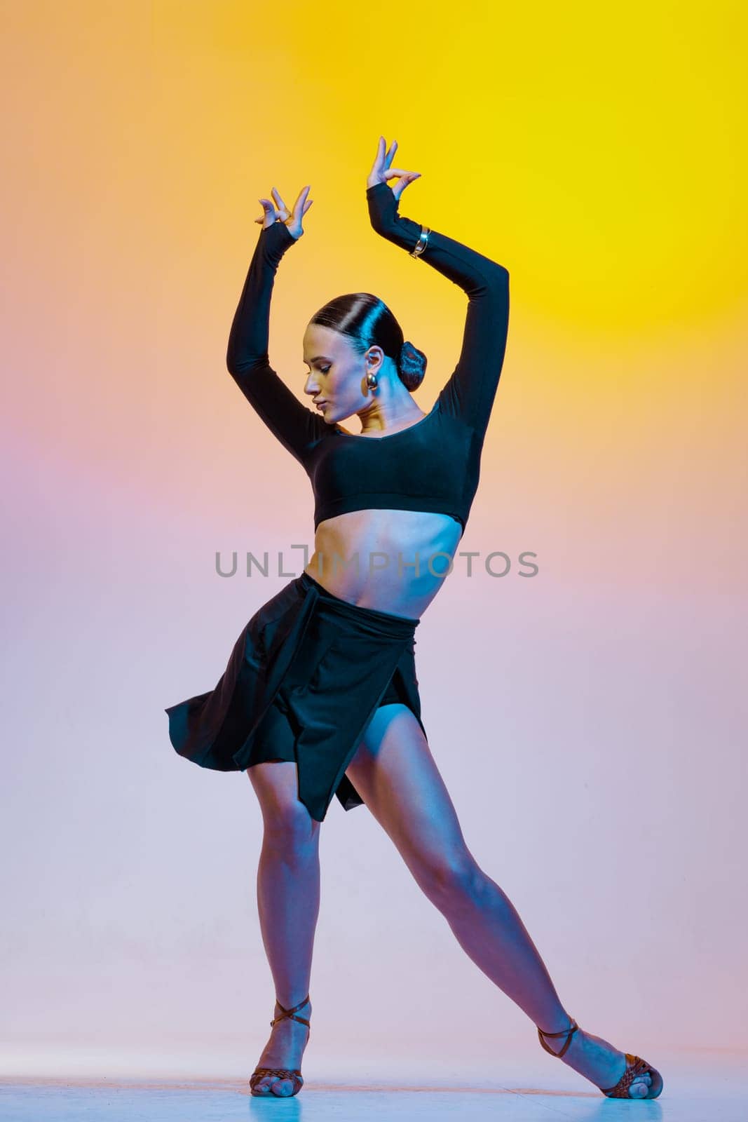 Stylish female dancer in black outfit posing in Latin dance move on vibrant gradient studio background.