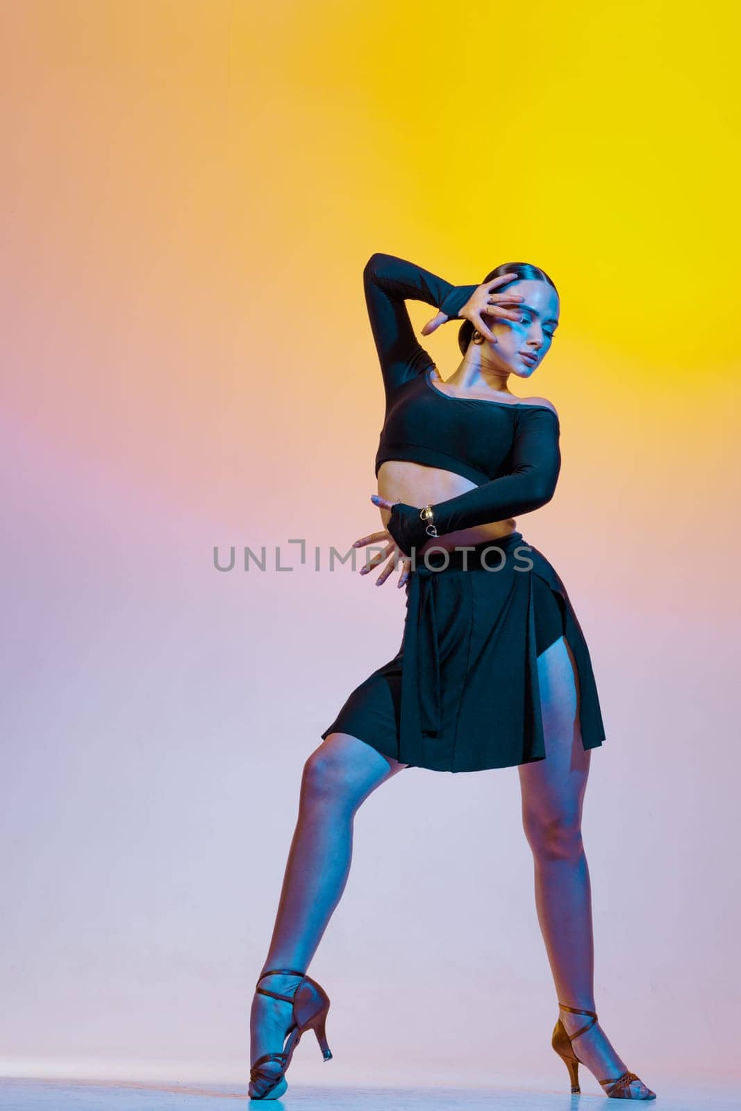 Graceful dancer in black clothes dances Latin American dances on a bright gradient background.