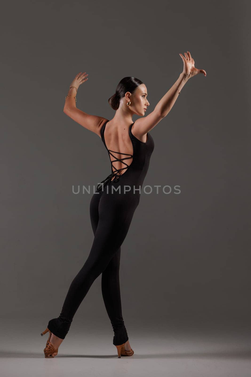 Female dancer in black bodysuit performing contemporary Latin dance pose on gray studio,