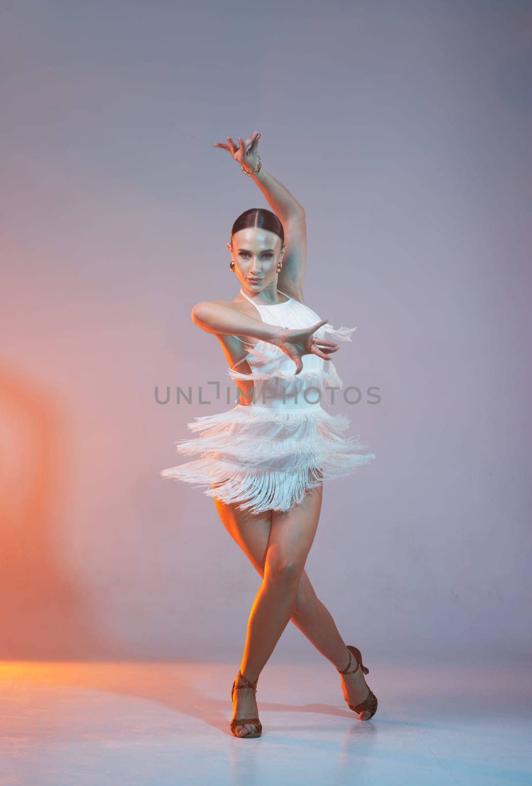 Elegant female Latin dancer in a white fringed dress performing a dynamic move with grace and confidence in artistic lighting.