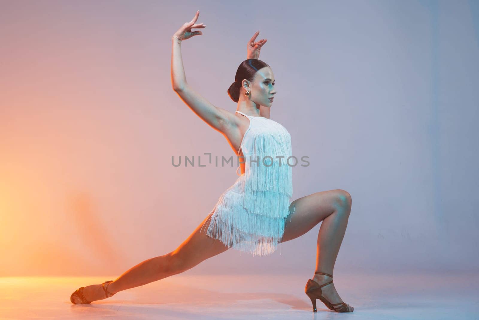 Elegant female Latin dancer in a white fringed dress performing a dynamic move with grace and confidence in artistic lighting.