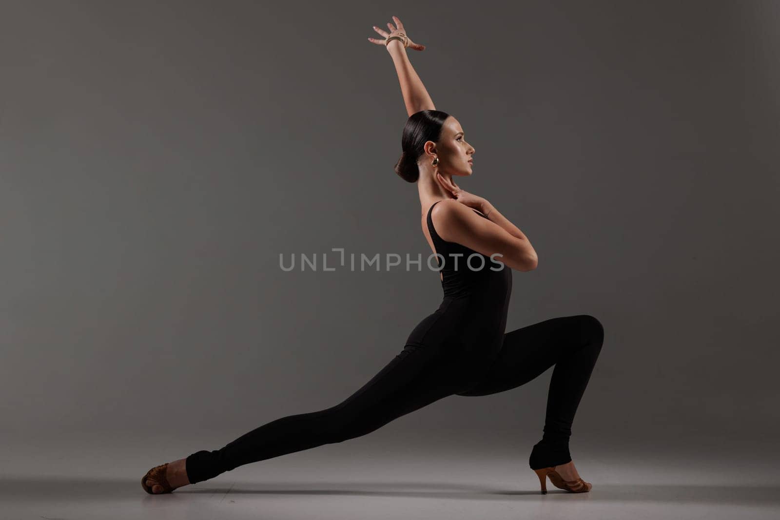 Female dancer in black bodysuit performing contemporary Latin dance pose on gray studio,