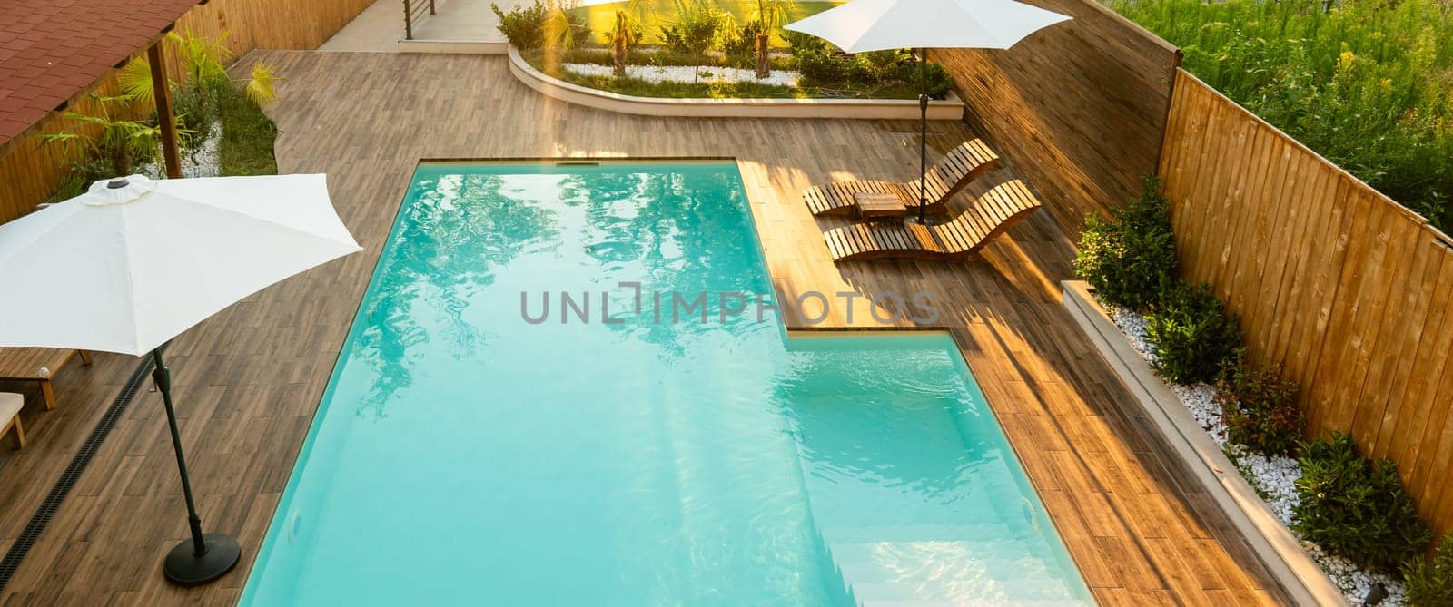 Modern swimming pool with turquoise water, wooden deck, umbrellas, and lounge chairs in a tranquil backyard