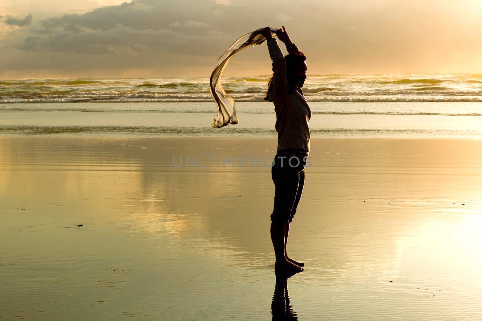 A woman lets a scarf blow in the wind at sunset on the beach in Newport, Oregon.