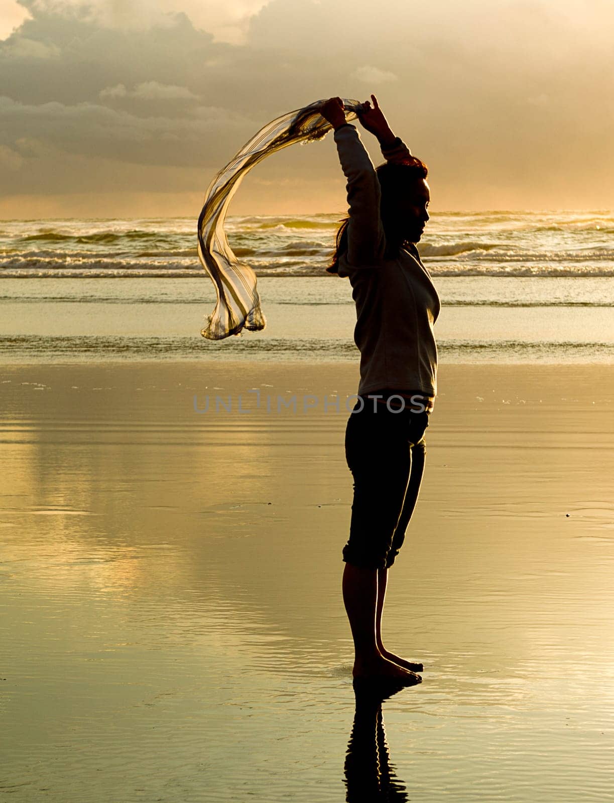 A woman lets a scarf blow in the wind at sunset on the beach in Newport, Oregon.