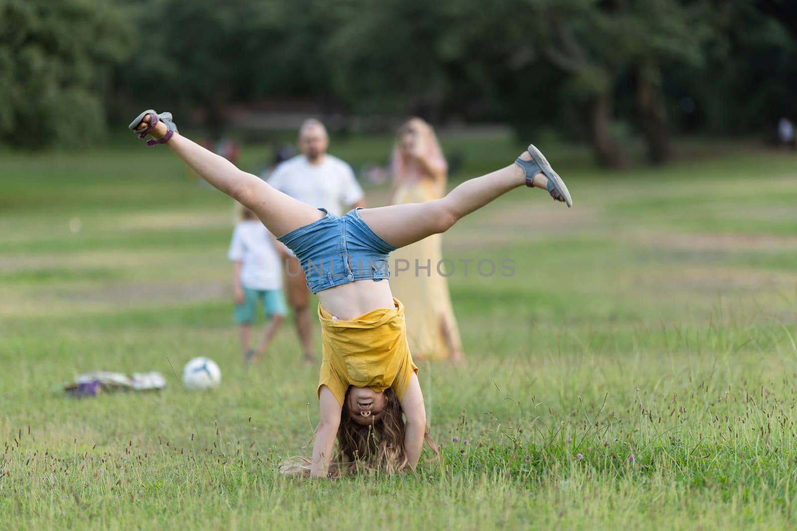 Girl practicing cartwheel in park with family watching, enjoying summer activity and healthy lifestyle