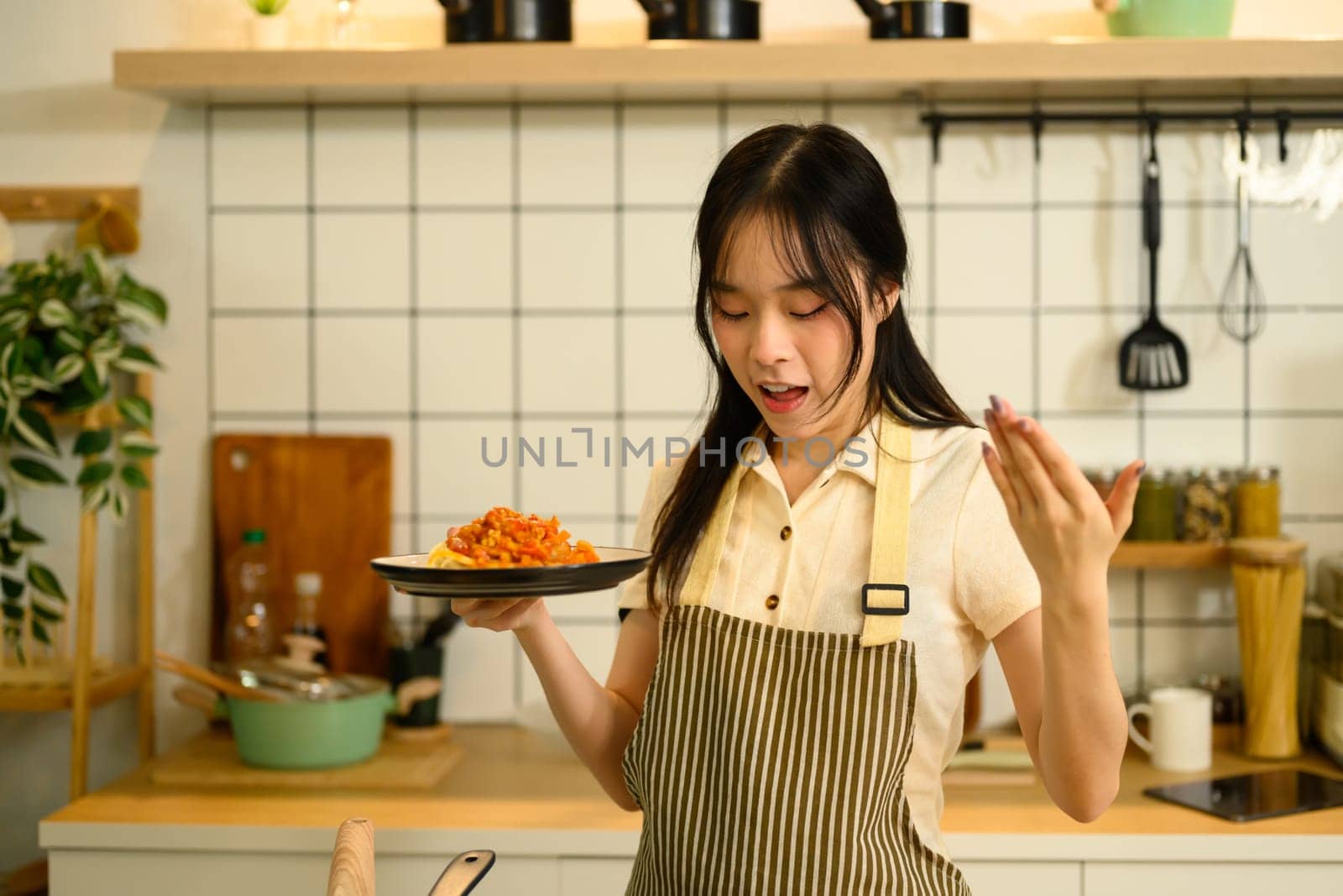 Young woman holding a freshly prepared plate of spaghetti with tomato sauce in her kitchen.