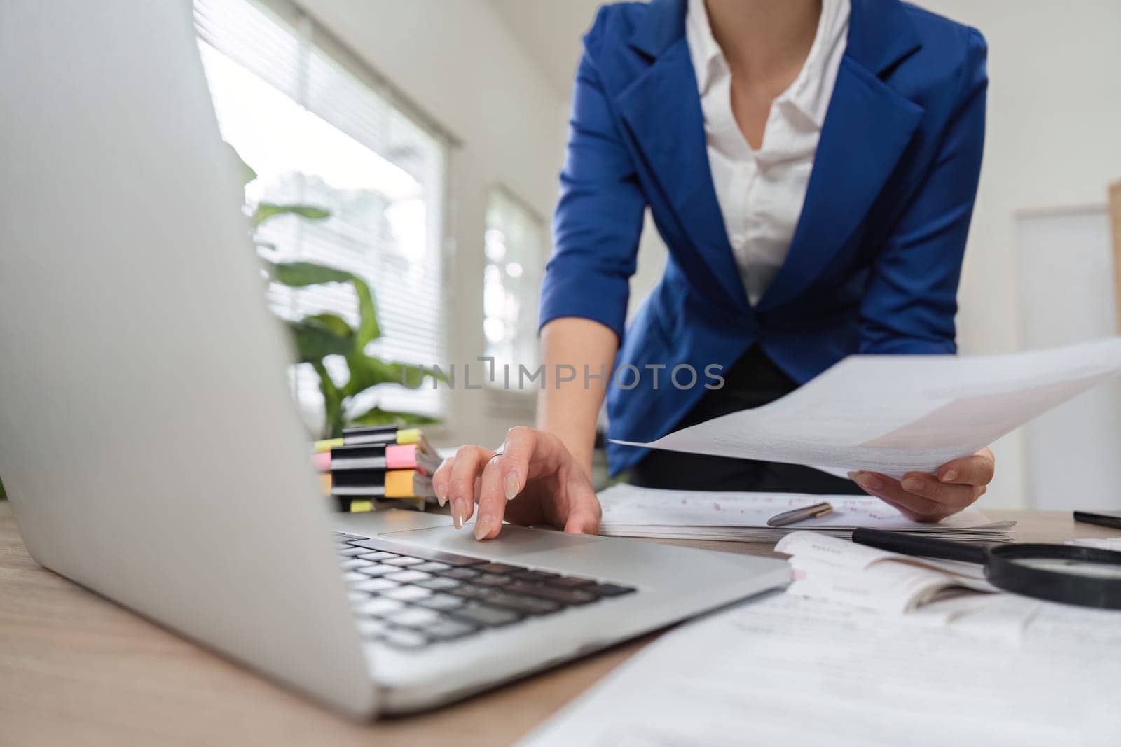 A professional businesswoman organizes tax documents and financial records while using a laptop in her office.