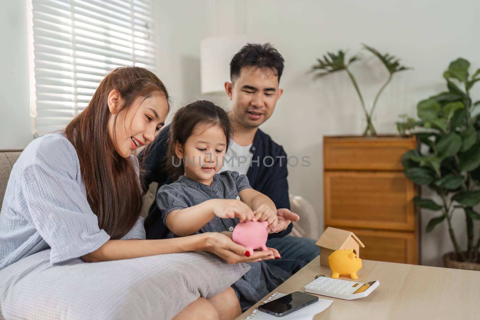 A family sits together, teaching their child about saving money using piggy banks and financial documents.