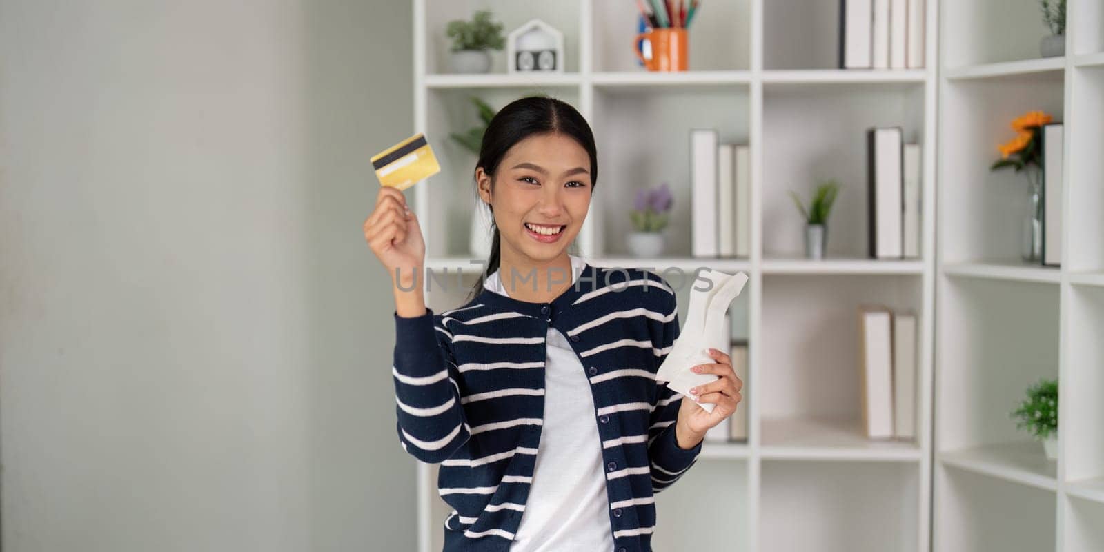 An enthusiastic woman holds up her credit card and a bill, celebrating her financial achievements.