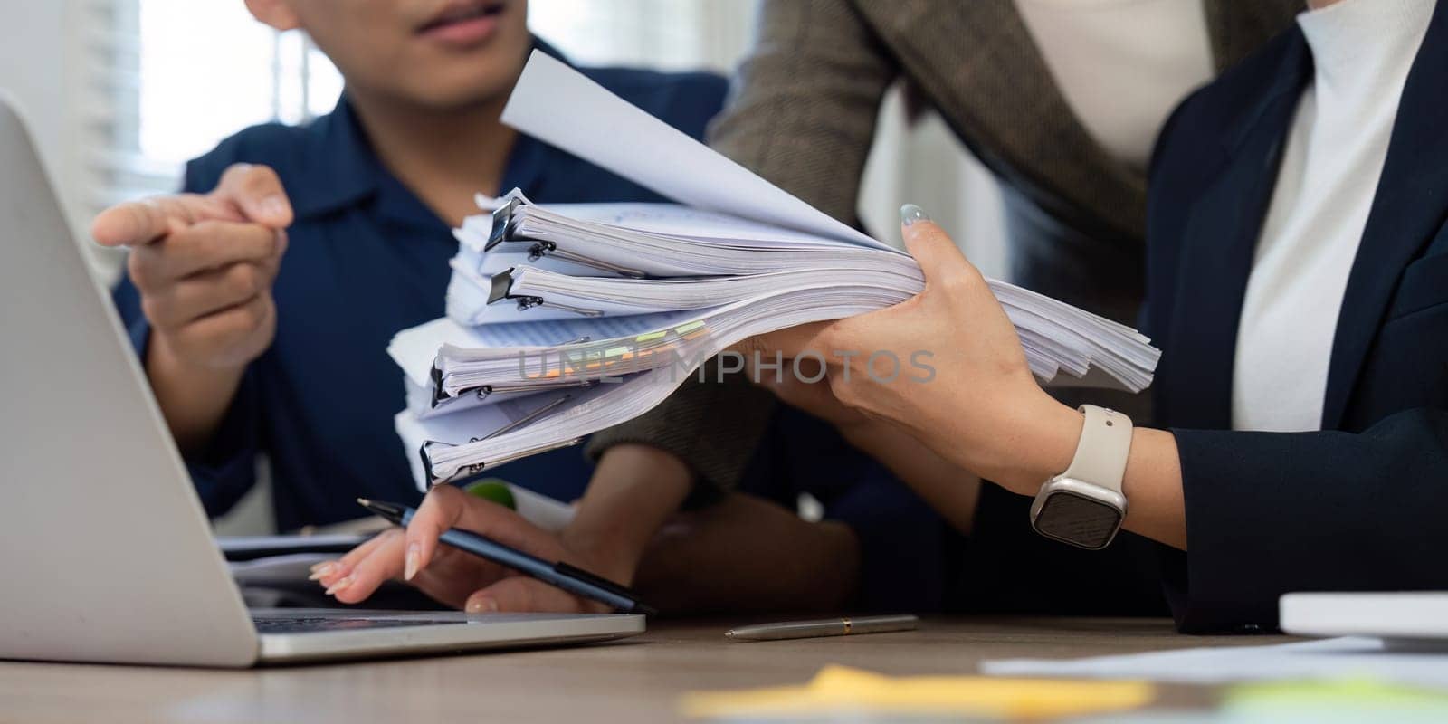 A group of professionals collaborates on paperwork and digital devices, demonstrating teamwork and effort in a busy office.