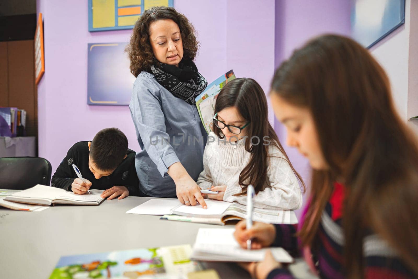 Female teacher helping elementary students at language school class.