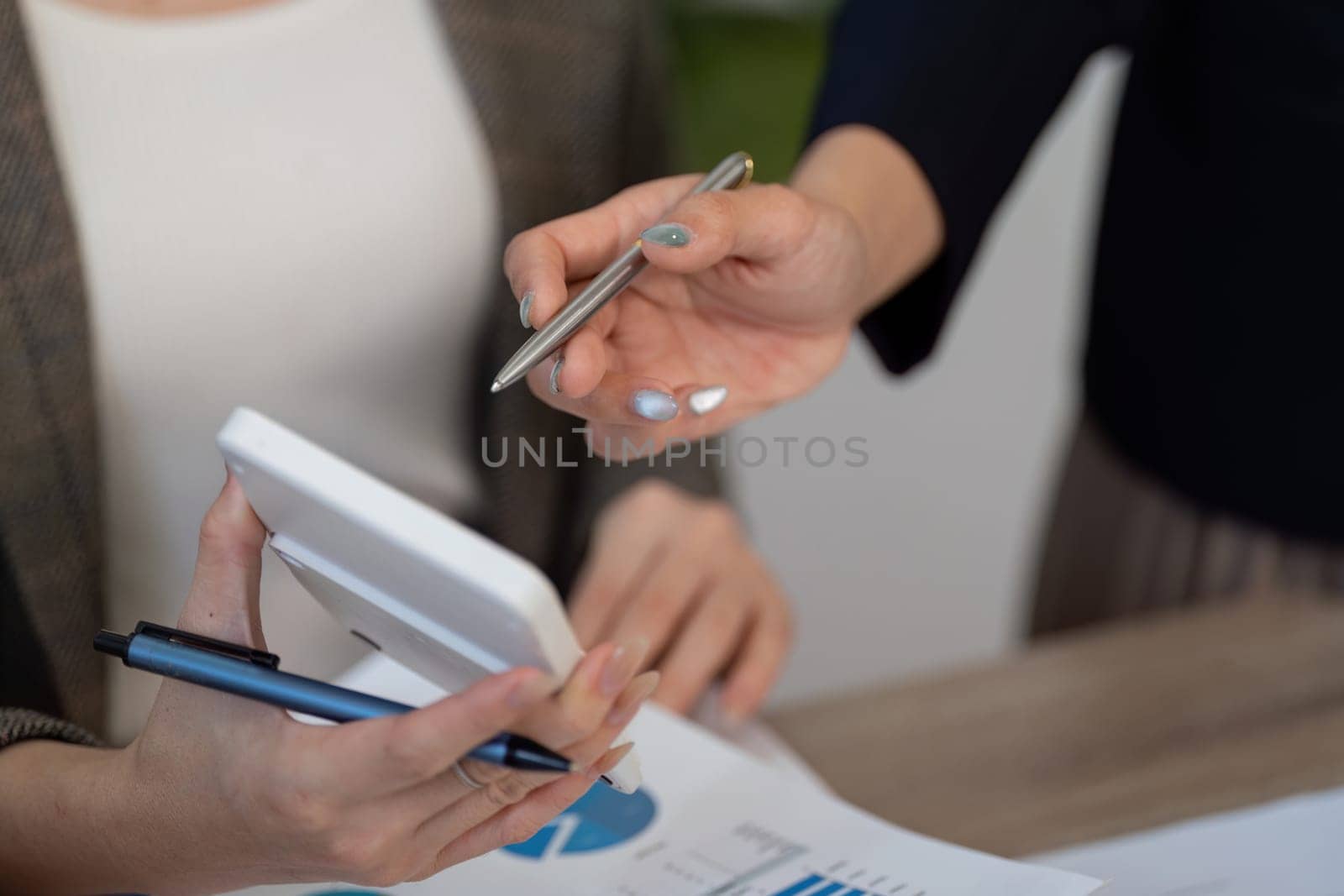 Two business professionals engage in a discussion, analyzing financial data on a tablet and reviewing documents.
