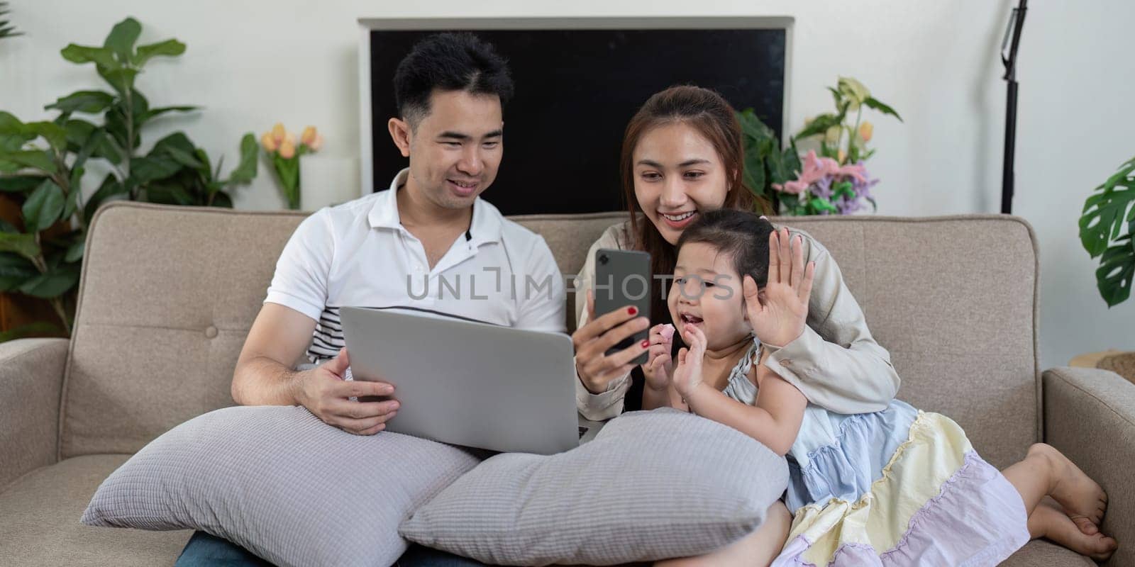 A family of three enjoys a video call on a smartphone, sharing smiles and playful gestures from their cozy couch.