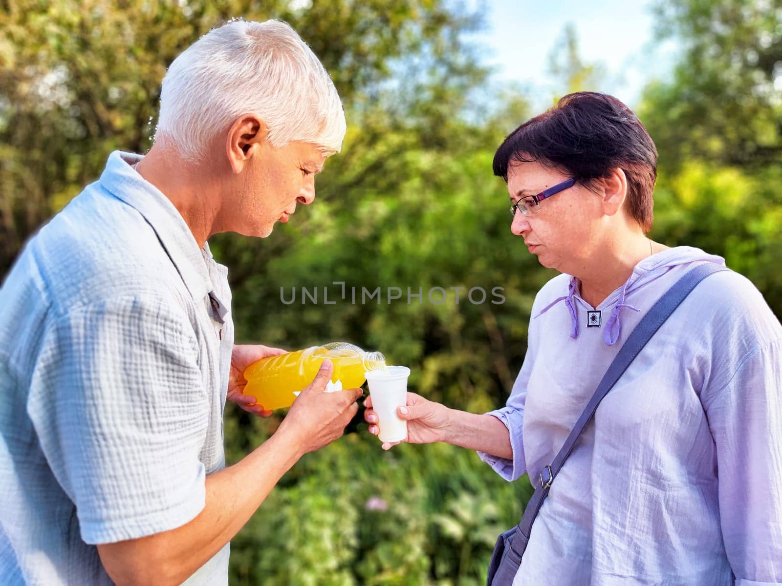 Two people share a drink in a lush garden, enjoying a warm day surrounded by greenery and nature.
