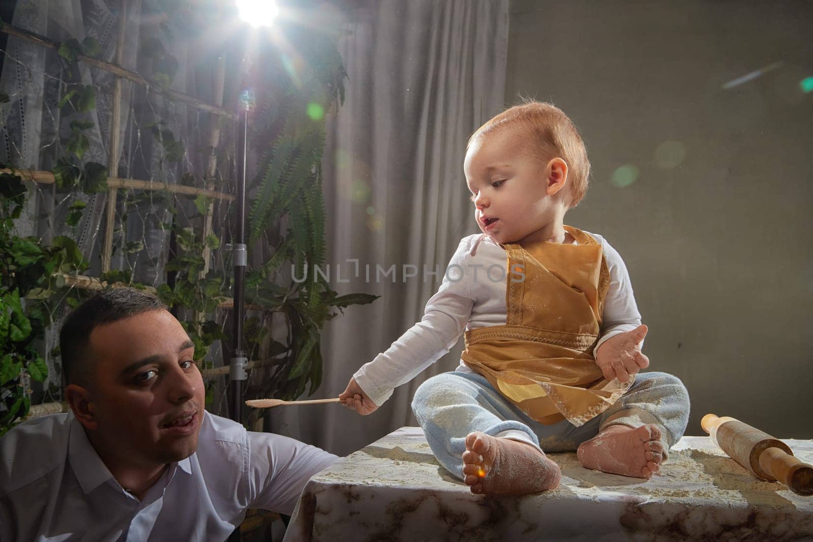 A family enjoys a fun cooking session, playfully covered in flour while engaging with their little ones in a warm kitchen. Father and son having fun