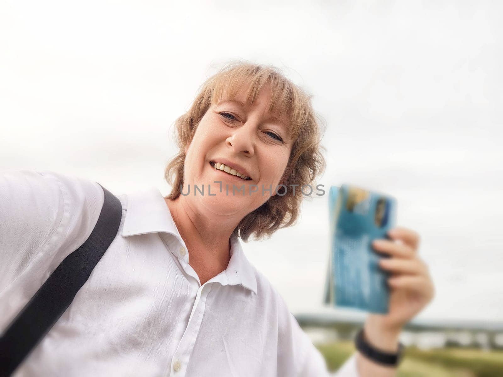 Middle-aged woman takes a joyful selfie while exploring a beautiful landscape on her travel excursion.