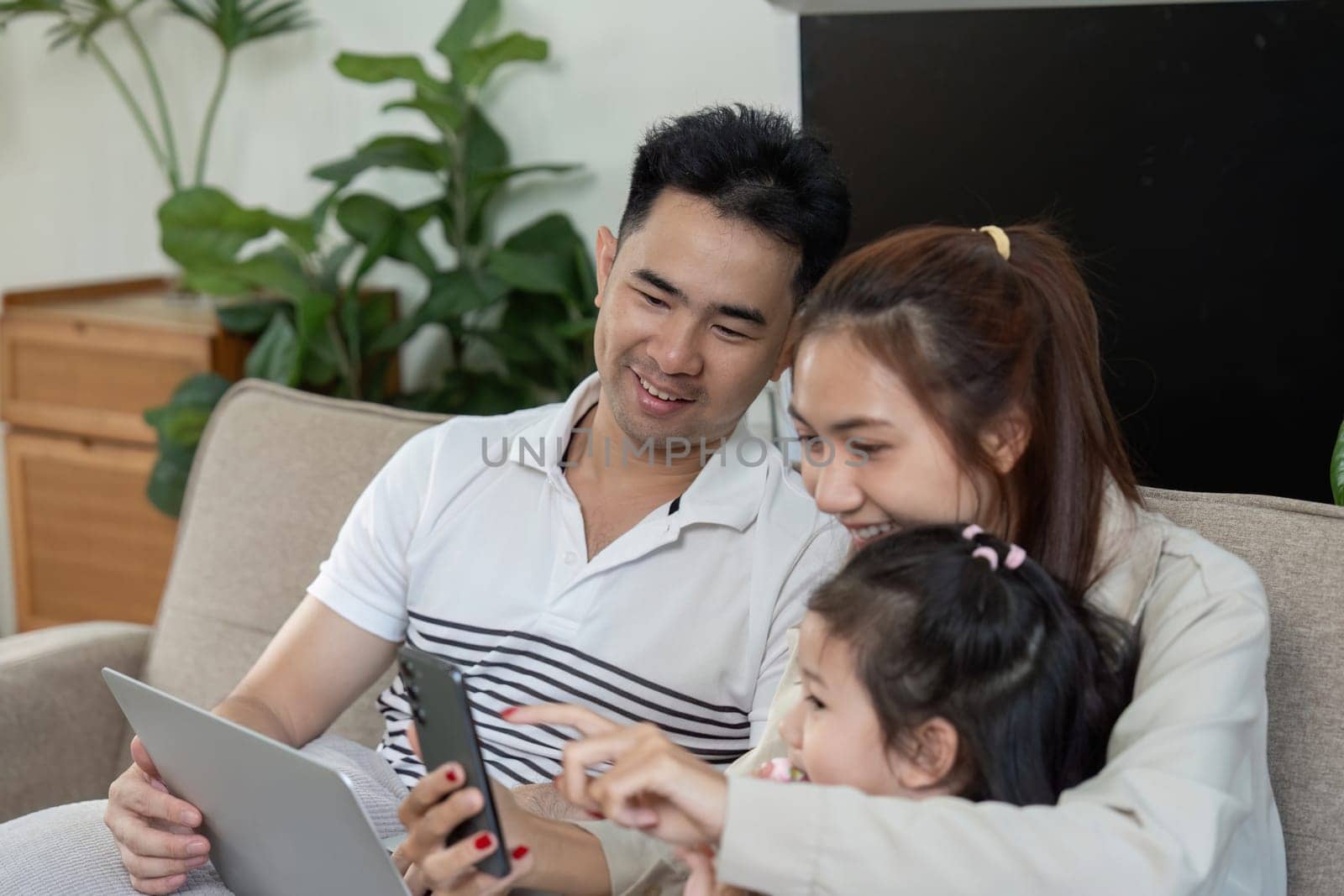 A family of three enjoys a playful moment on the couch, sharing laughter while using their devices.