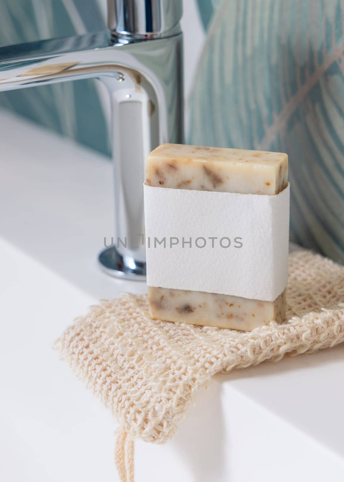 Beige handmade soap bar with blank label on sisal soap saver bag on washbasin close up, packaging mockup, copy space. Natural herbal unbranded product for daily hygiene