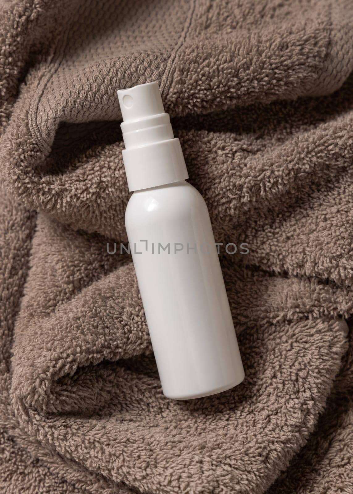 White blank spray cream bottle on brown towel in bathroom top view, brand packaging mockup. Natural herbal cosmetic product - cream, lotion or foam for daily facecare, copy space