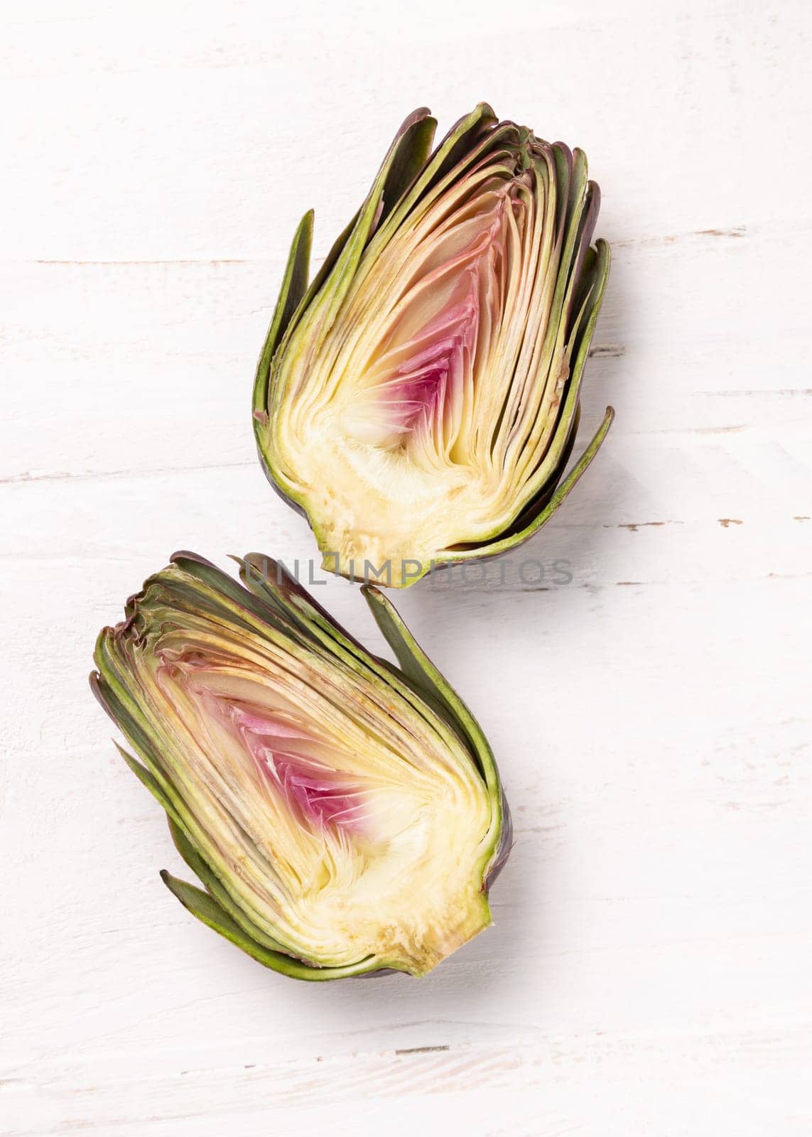 Purple raw roman artichoke cut in half on a white wooden table top view, copy sapce. Fresh vegetables bought on farmers market ready to cook. Italian cousine ingredient