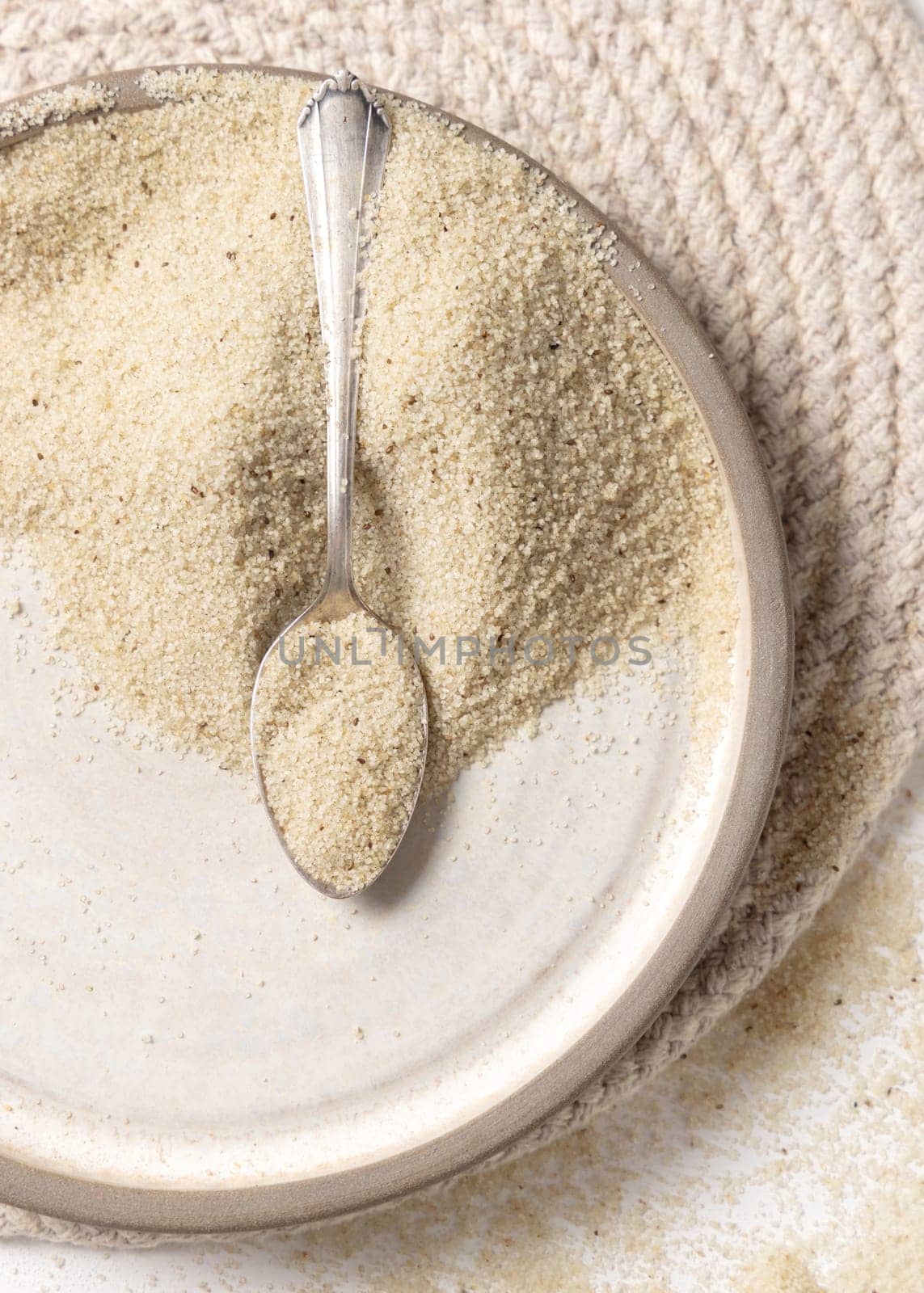 Raw uncooked fonio seeds in a plate with a metal spoon on white table top view, copy space. African ancient pseudocereal. Organic super food. Healthy food concept. Gluten free alternative seeds