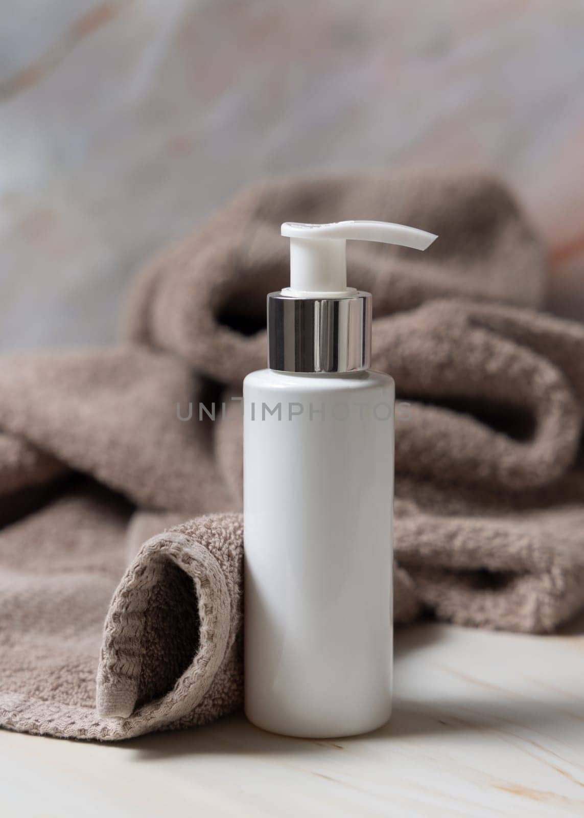 White blank one pump cream bottle near brown towel in bathroom closeup, brand packaging mockup. Natural herbal cosmetic product - cream, lotion or foam for daily facecare, copy space