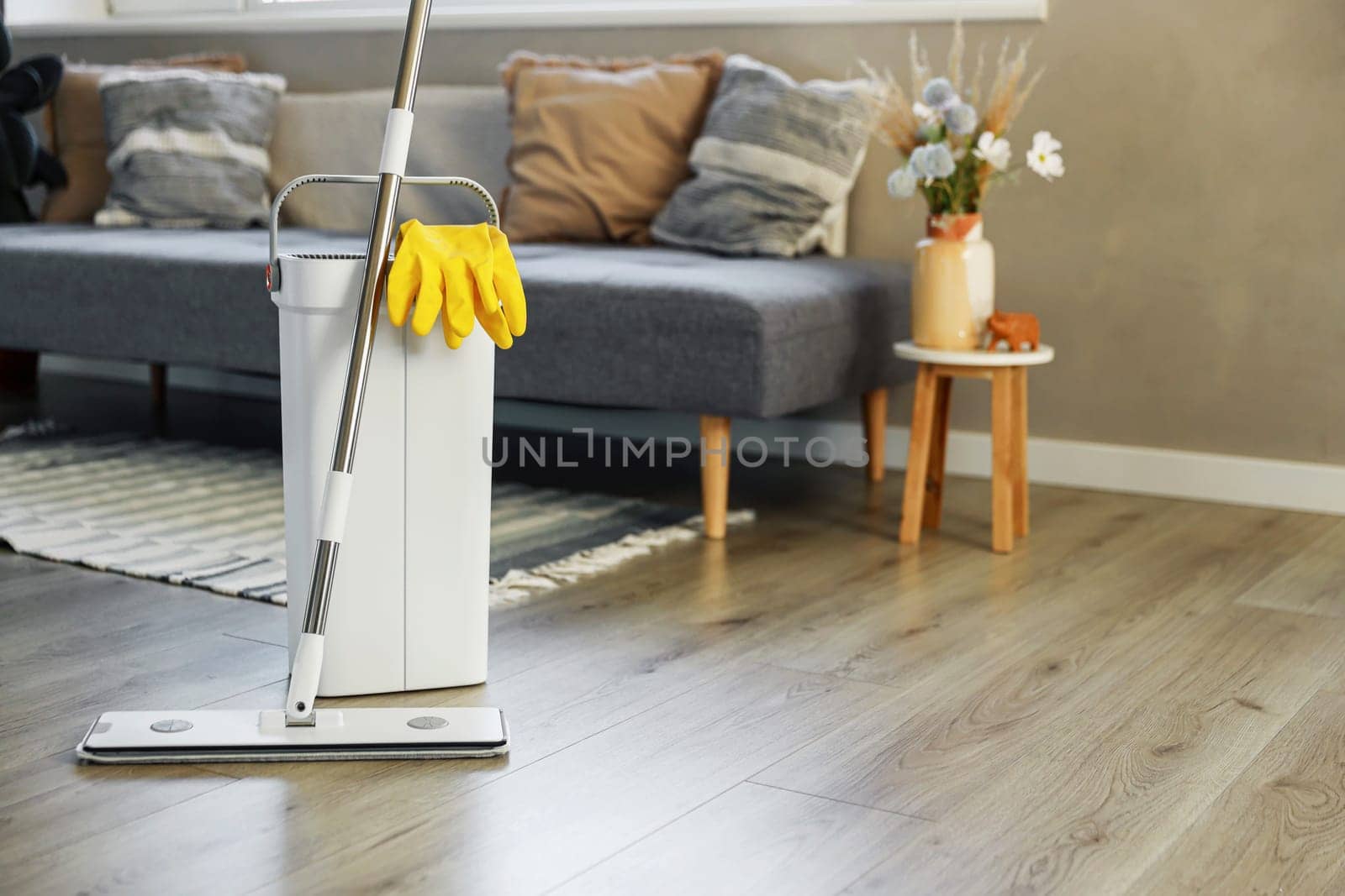 Cleaning supplies: mop, gloves, bucket with wringer sitting on wooden laminate floor in modern living room, wet equipment tools, housekeeping concept. Emphasizing home sanitation, cleanliness, hygiene
