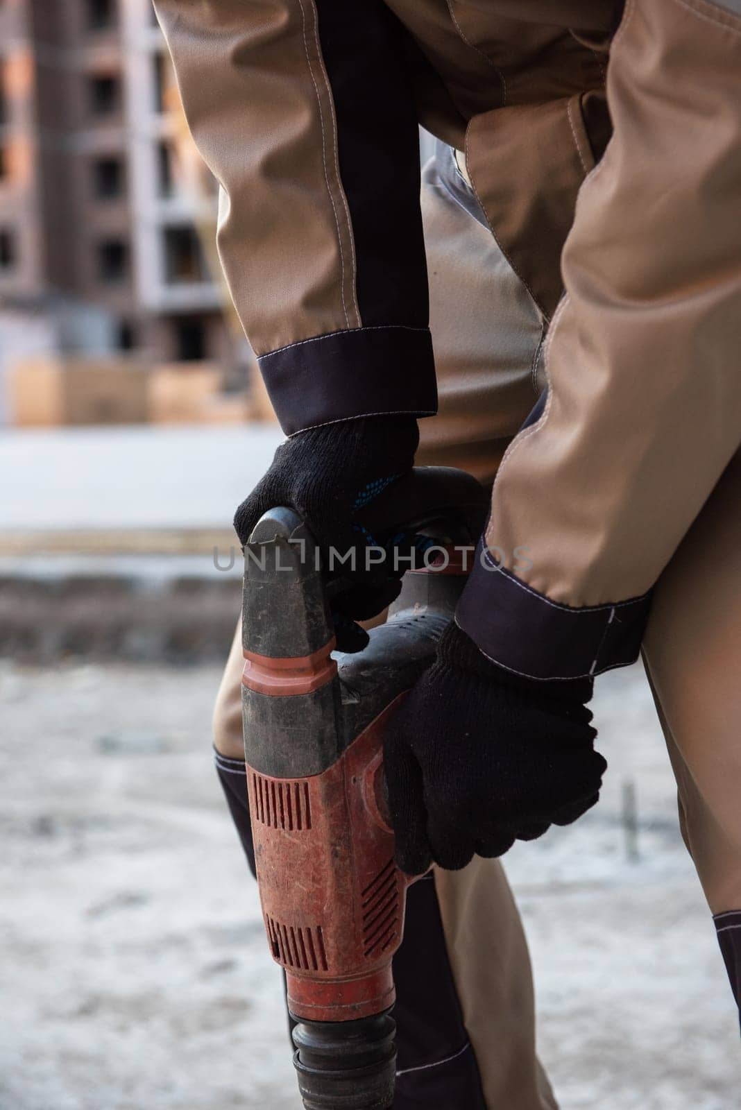 Close-up of a construction worker operating a power drill on a building site, wearing safety gear and work boots.