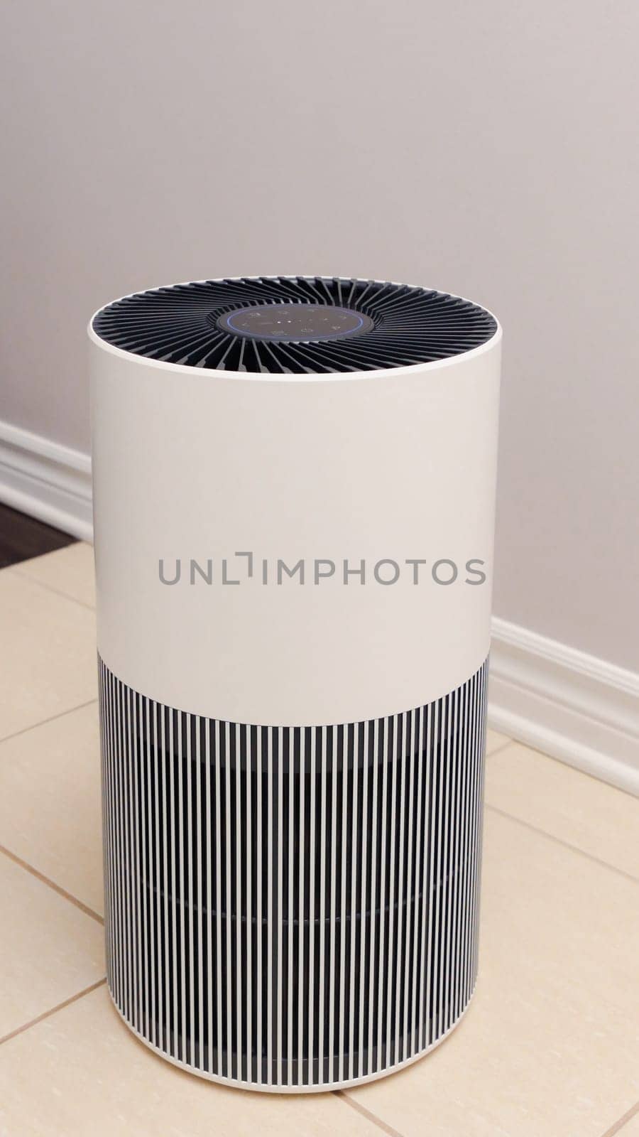 Tall round air purifier with a black top fan and a white body on a tile floor against the wall.