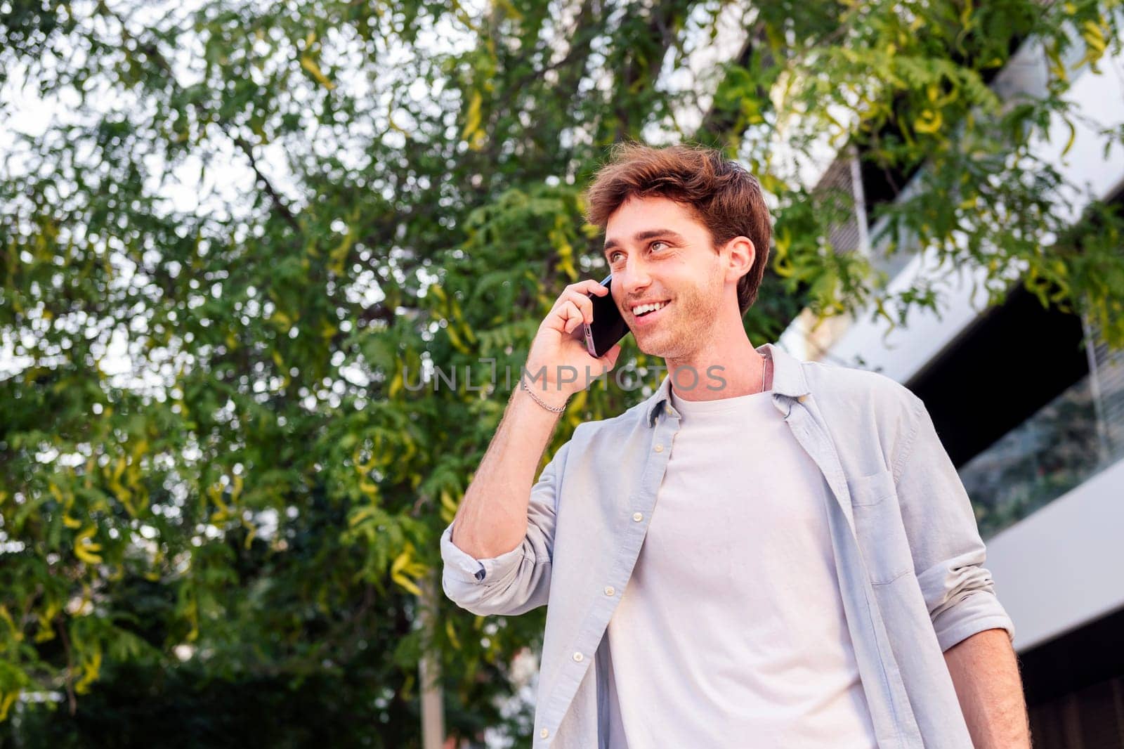 young man smiling happy while walking down the street in a good mood talking on mobile phone, concept of technology of communication and urban lifestyle, copyspace for text